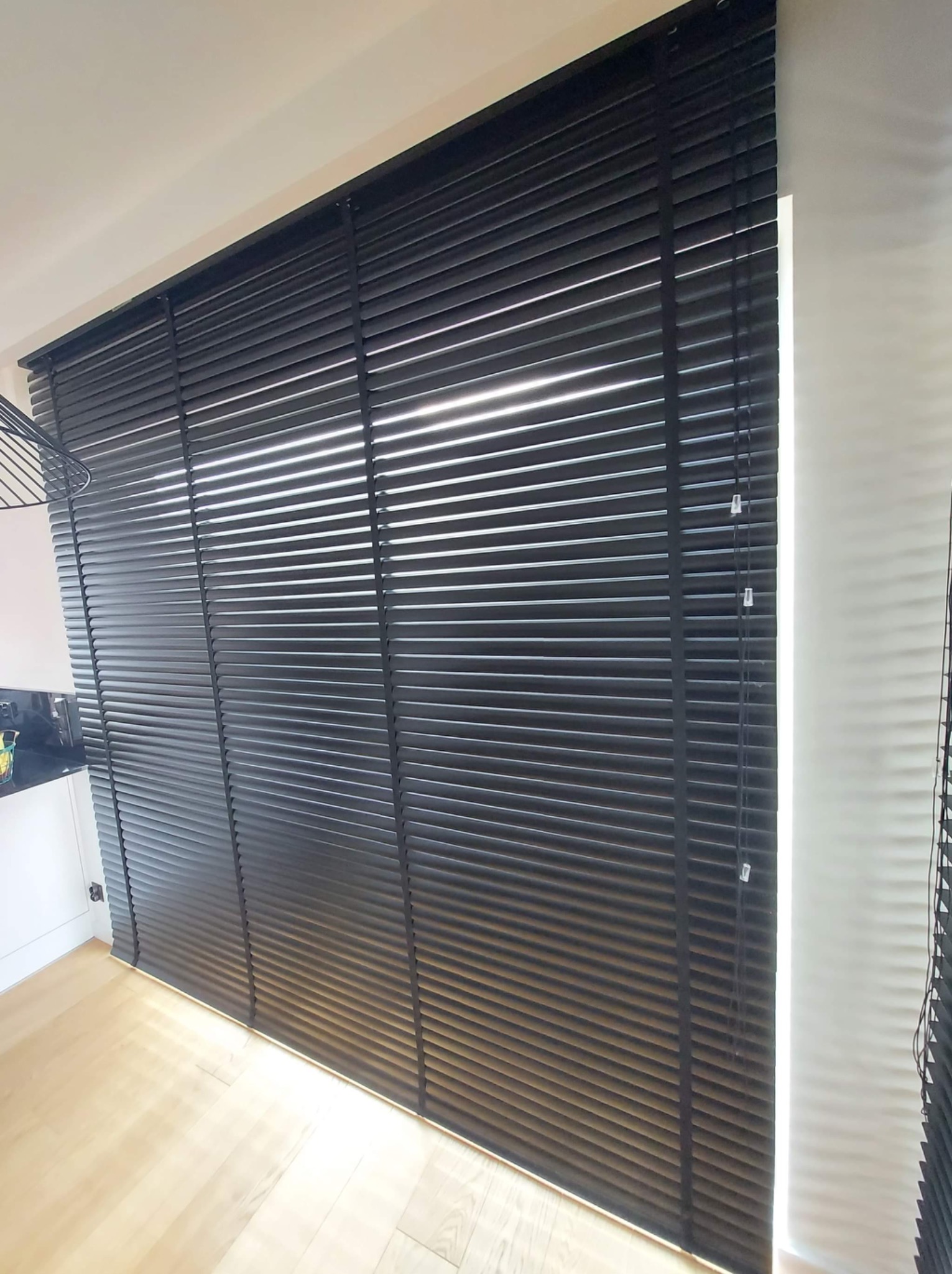 Czarne żaluzje aluminiowe zamontowane w oknie w Zambrowie, z widocznym fragmentem blatu kuchennego w tle.