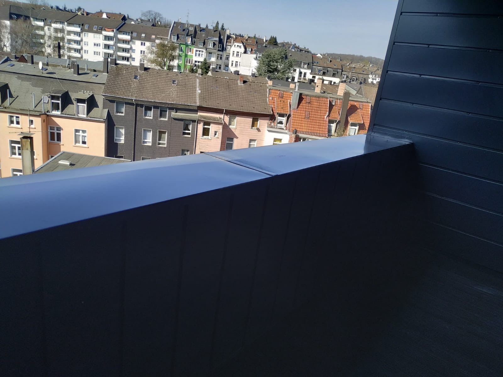 Nowoczesne, grafitowe wykończenie dachu z blachy na tle zabudowy miejskiej z różnorodnymi dachami.