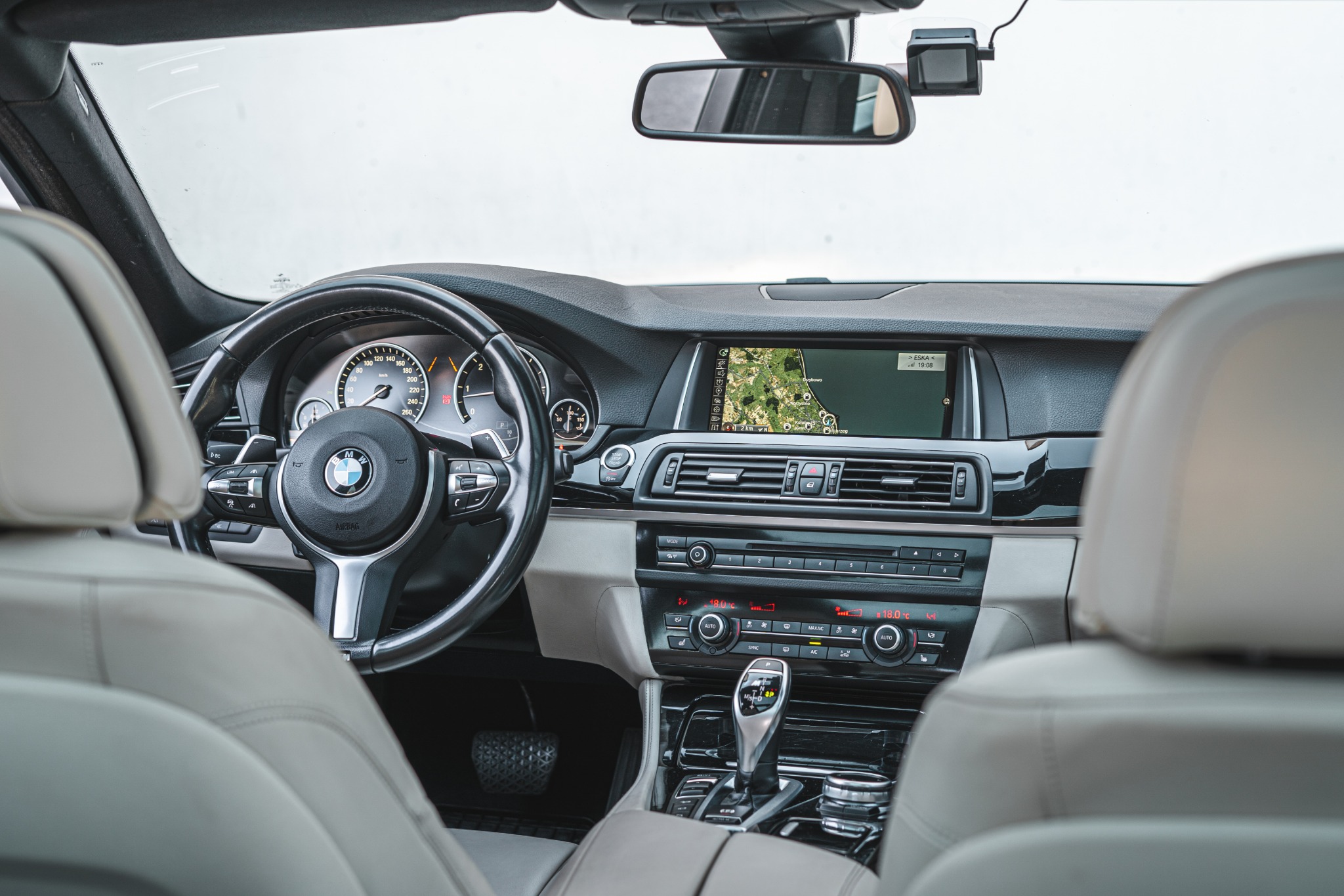 Wnętrze samochodu BMW z widoczną nawigacją GPS, skórzaną kierownicą i automatyczną skrzynią biegów, sfotografowane z tylnych siedzeń.