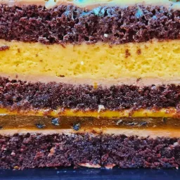 Przekrój tortu czekoladowego z warstwami biszkoptu, kremu pomarańczowego, konfitury mango-marakuja i karmelu z mango, prezentujący bogactwo tekstur i smaków.