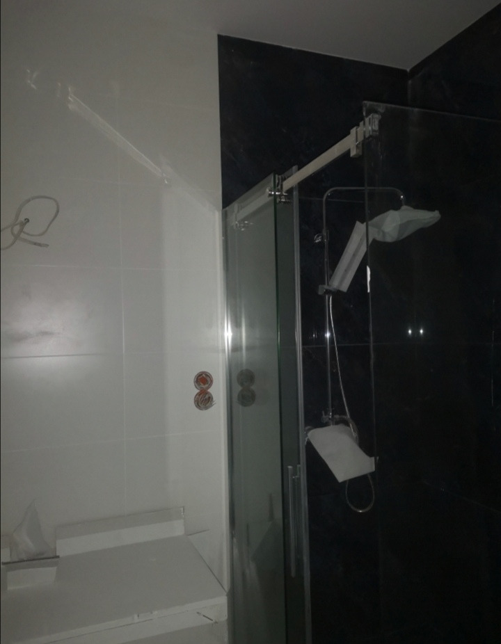 Nowoczesna kabina prysznicowa z przesuwnymi drzwiami na tle czarnych i białych płytek, widoczne włączniki światła na białej ścianie.