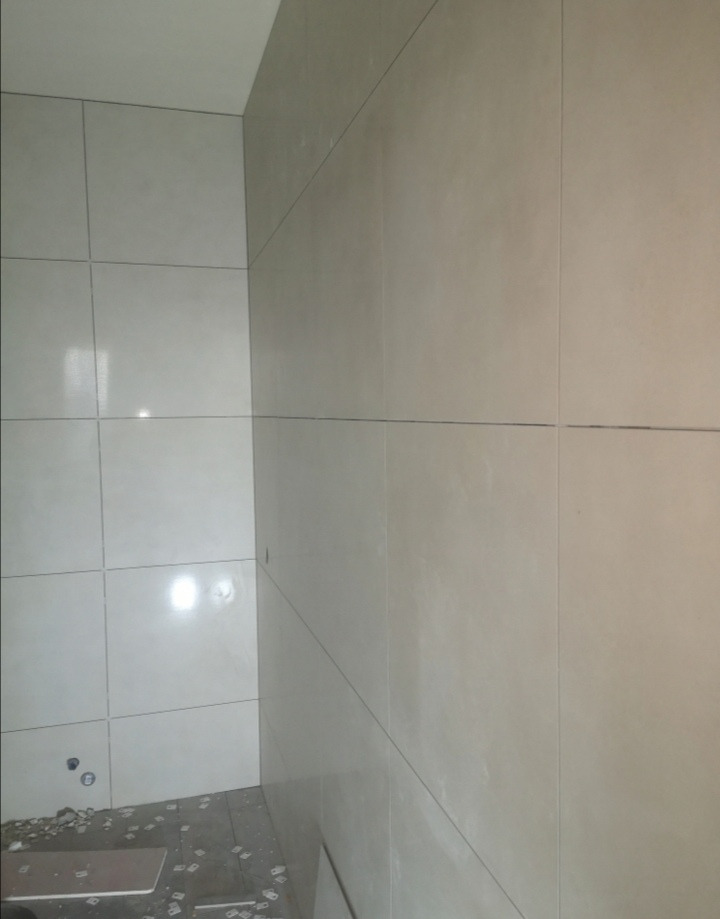 Świeżo położone, jasne płytki ceramiczne na ścianach w rogu łazienki, widoczne pozostałości po pracach glazurniczych na podłodze.