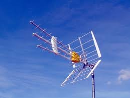 Antena telewizyjna zamontowana na maszcie, widoczna na tle błękitnego nieba. Na antenie widoczna pomarańczowa osłona. Ujęcie z dołu.