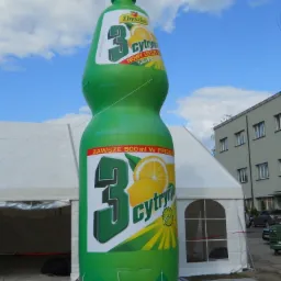 Dmuchana reklama w kształcie butelki napoju '3 Cytryny' marki Zbyszko, umieszczona przed białym namiotem imprezowym.