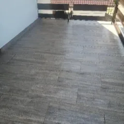 Szare płytki imitujące drewno na balkonie z metalową balustradą i widokiem na dach budynku.