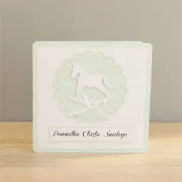 Ręcznie robiona kartka z okazji Chrztu Świętego, z wyciętym konikiem na biegunach i napisem 'Pamiątka Chrztu Świętego', pastelowe kolory i delikatne zdobienia.