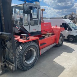 FS-Lechowicz Krzysztof Lechowicz - Czerwono-biały wózek widłowy Kalmar DC18 na betonowym placu, z widoczną kabiną operatora i masywnymi oponami, na tle białego samochodu dostawczego i częściowo zachmurzonego nieba.