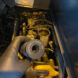 FS-Lechowicz Krzysztof Lechowicz - Osoba w czarnej rękawicy trzyma filtr Jungheinrich nad otwartym silnikiem wózka widłowego, widoczne elementy silnika i osprzętu.