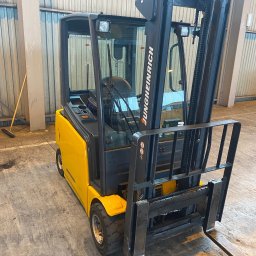 FS-Lechowicz Krzysztof Lechowicz - Żółto-czarny wózek widłowy Jungheinrich z kabiną, stojący w hali magazynowej, widok od tyłu.