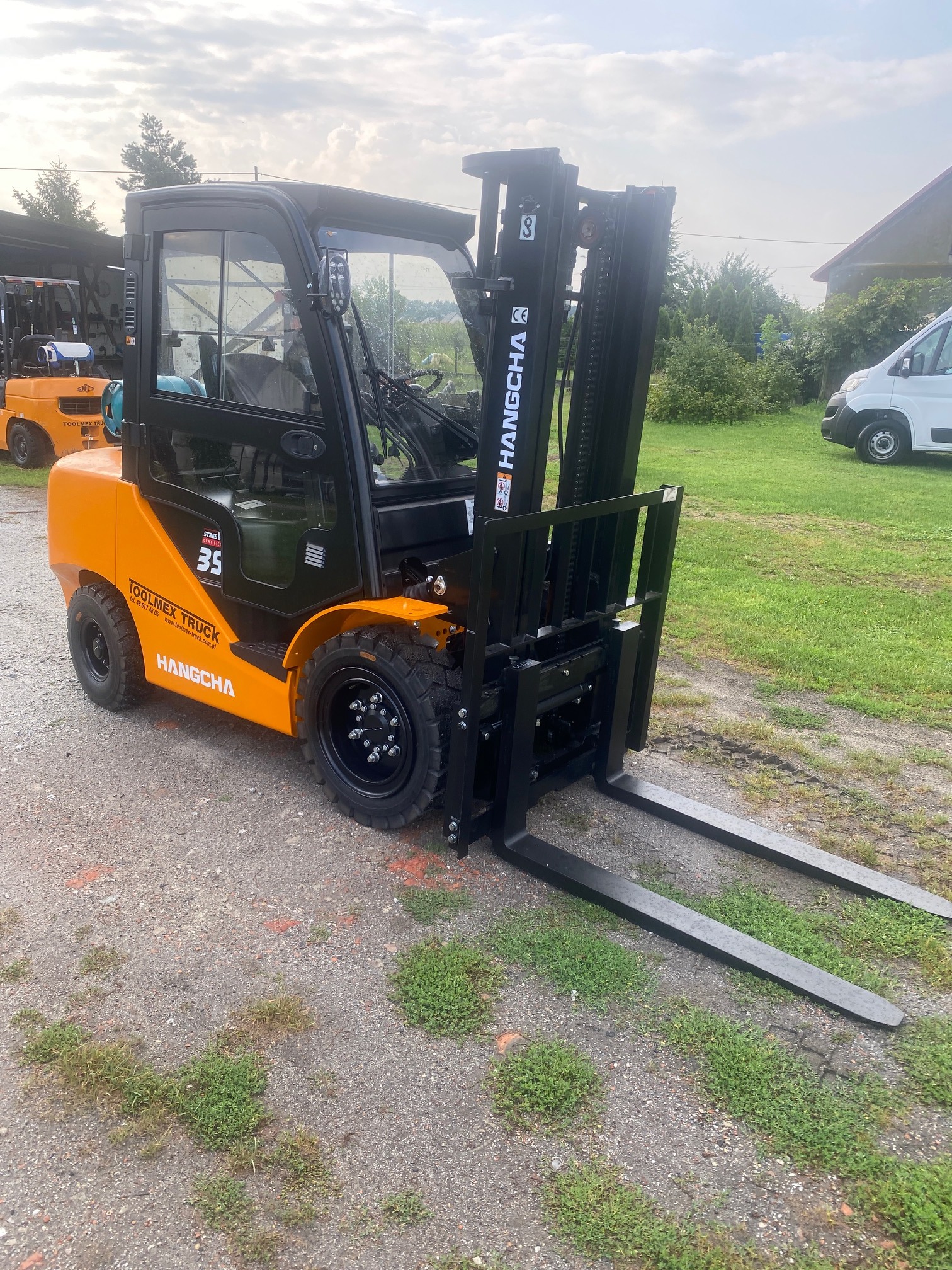 Nowy wózek widłowy spalinowy marki Hangcha w kolorze pomarańczowo-czarnym, model 3.5, stojący na żwirowym podłożu z widocznym logo Toolmex Truck.