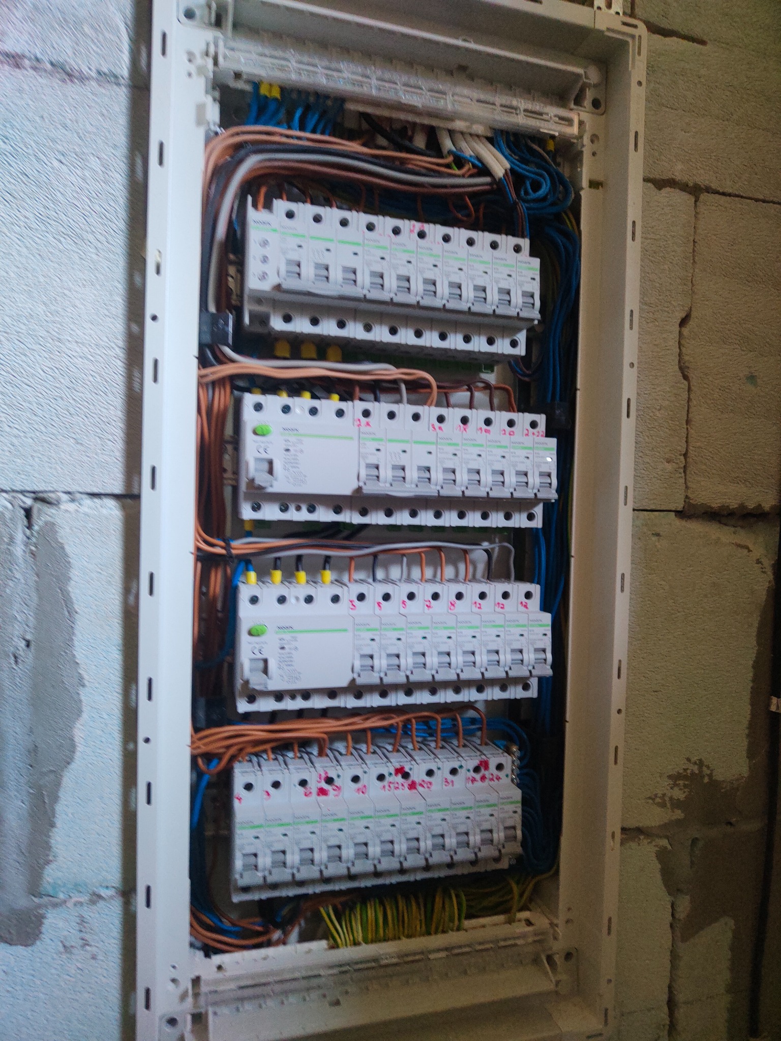 Rozdzielnica elektryczna z zamontowanymi bezpiecznikami i okablowaniem, widoczna na tle surowej ściany z betonu komórkowego.