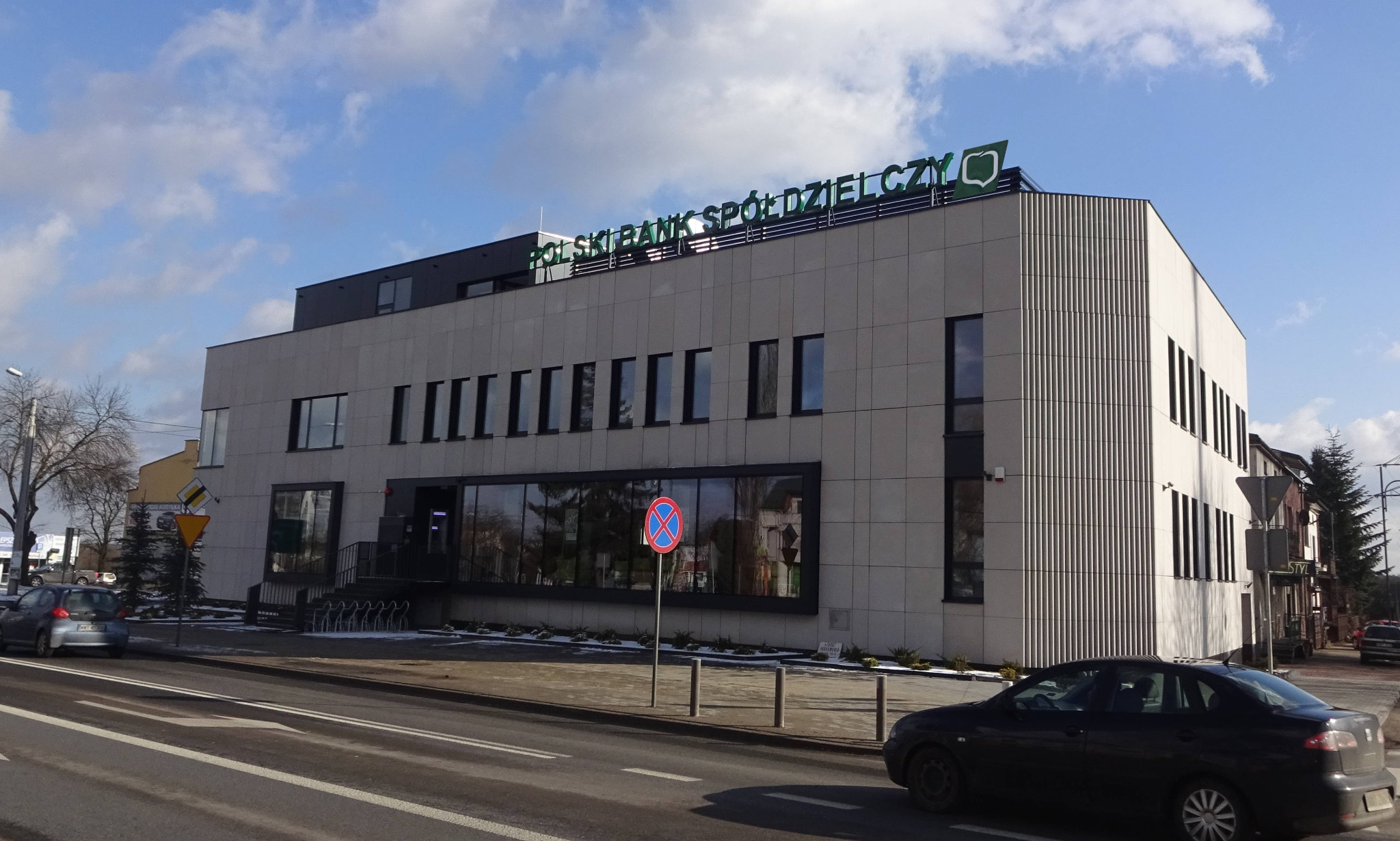 Zmodernizowany budynek Banku Spółdzielczego w Wyszkowie z elewacją z piaskowca i płyty kompozytowej, widok z ulicy w słoneczny dzień.