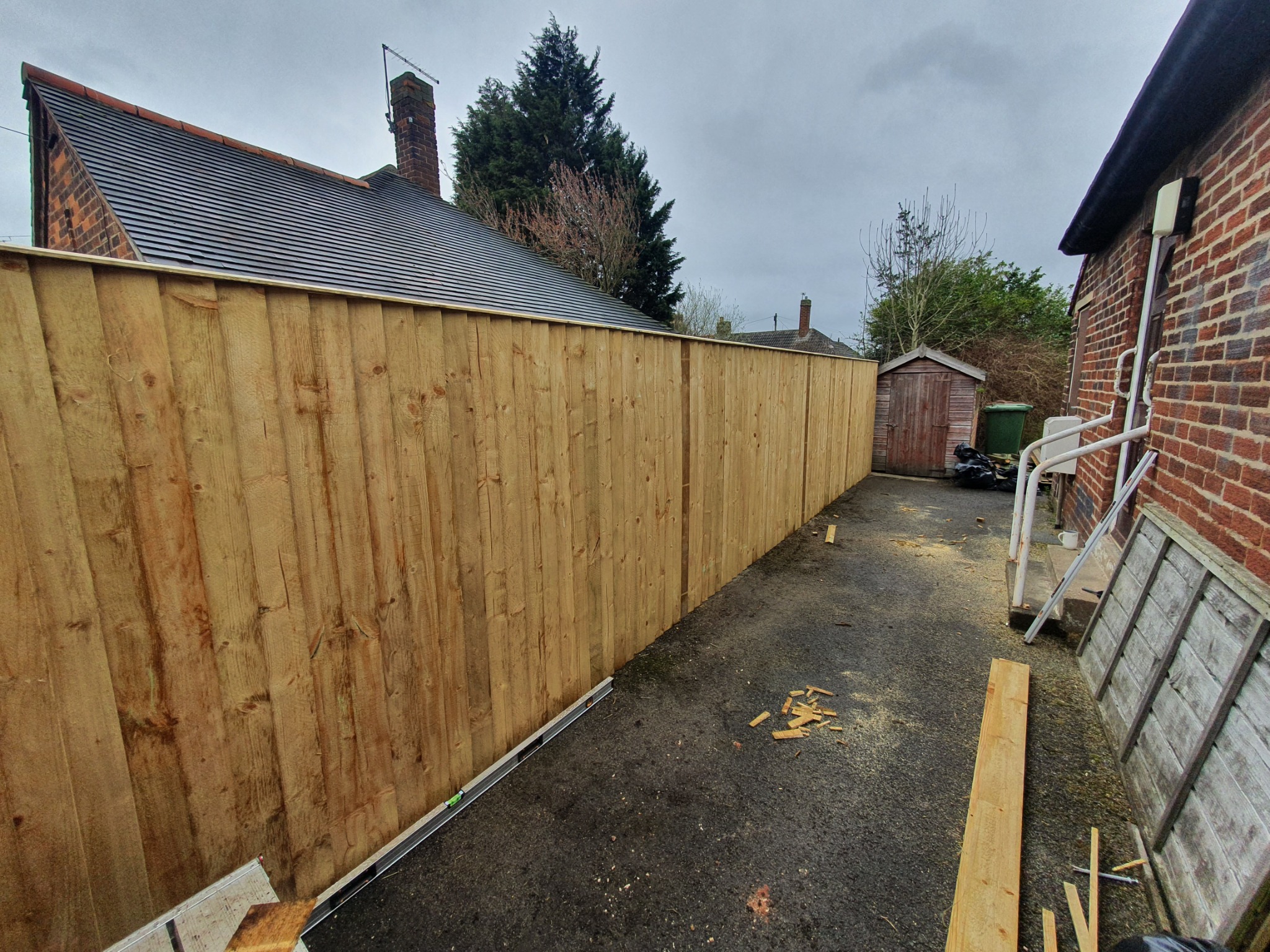 Nowo postawione, wysokie ogrodzenie z jasnego drewna, widoczne z perspektywy podwórka z rozrzuconymi wiórami, poziomica oparta o ogrodzenie.