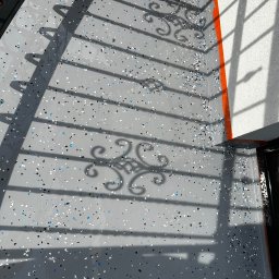 PHO HOME - Szara posadzka z kolorowymi płatkami na balkonie, cień ozdobnej balustrady, pomarańczowe wykończenie przy ścianie.