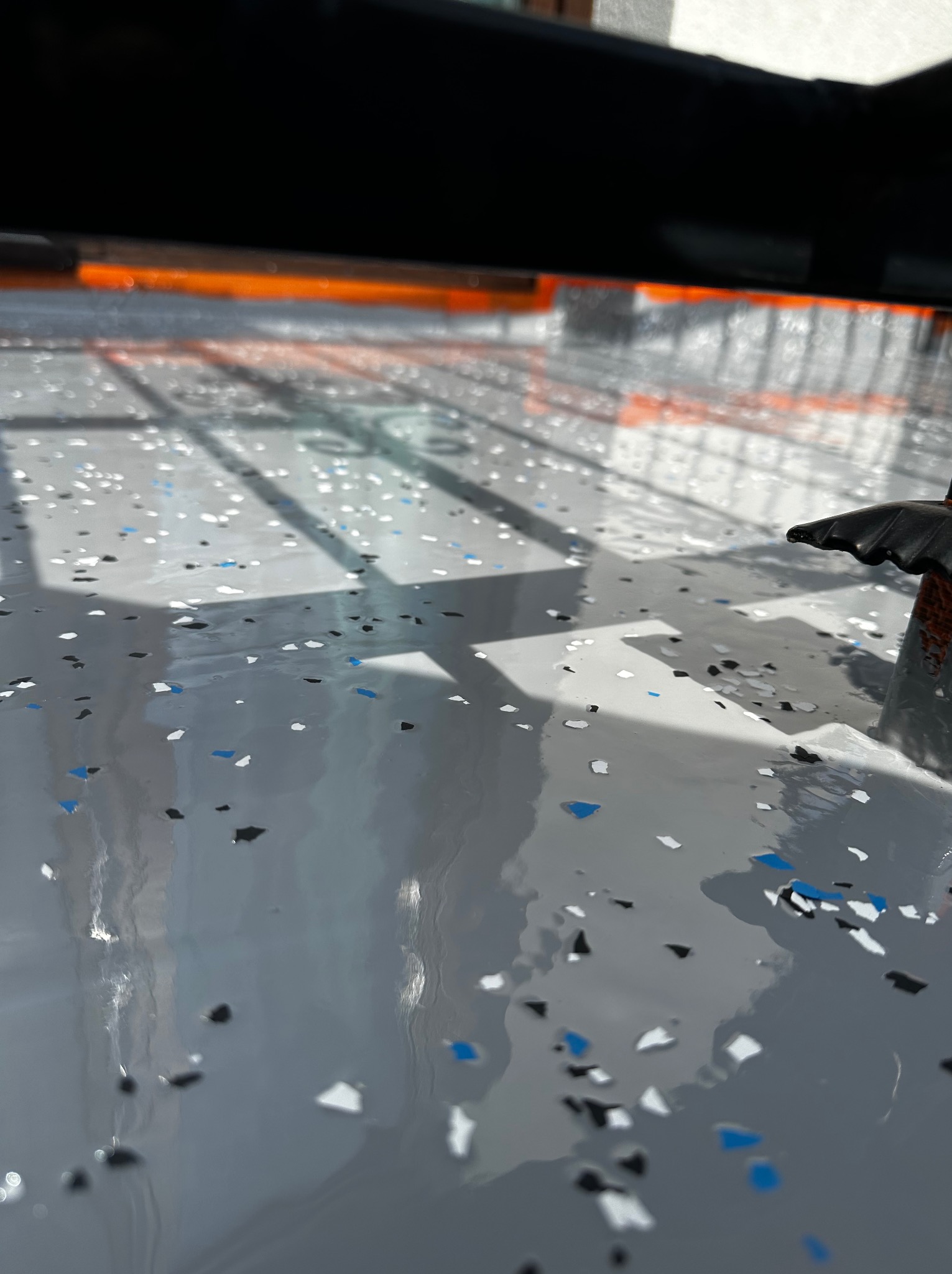 Świeżo wylana, szara posadzka z kolorowymi płatkami, widoczne refleksy światła i cień konstrukcji nad nią.