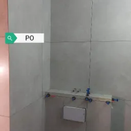 Świeżo ułożone, duże, szare płytki na ścianach w łazience, widoczne otwory na rury i stelaż podtynkowy, na suficie widoczne ślady po zalaniu.