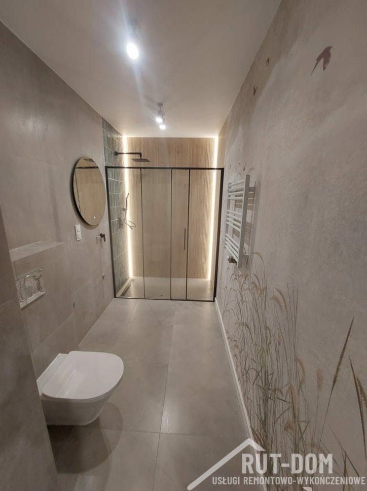 Nowoczesna łazienka z kabiną prysznicową typu walk-in z czarnymi ramami, podświetleniem LED, toaletą podwieszaną i ścianą z motywem trawy i ptaków.