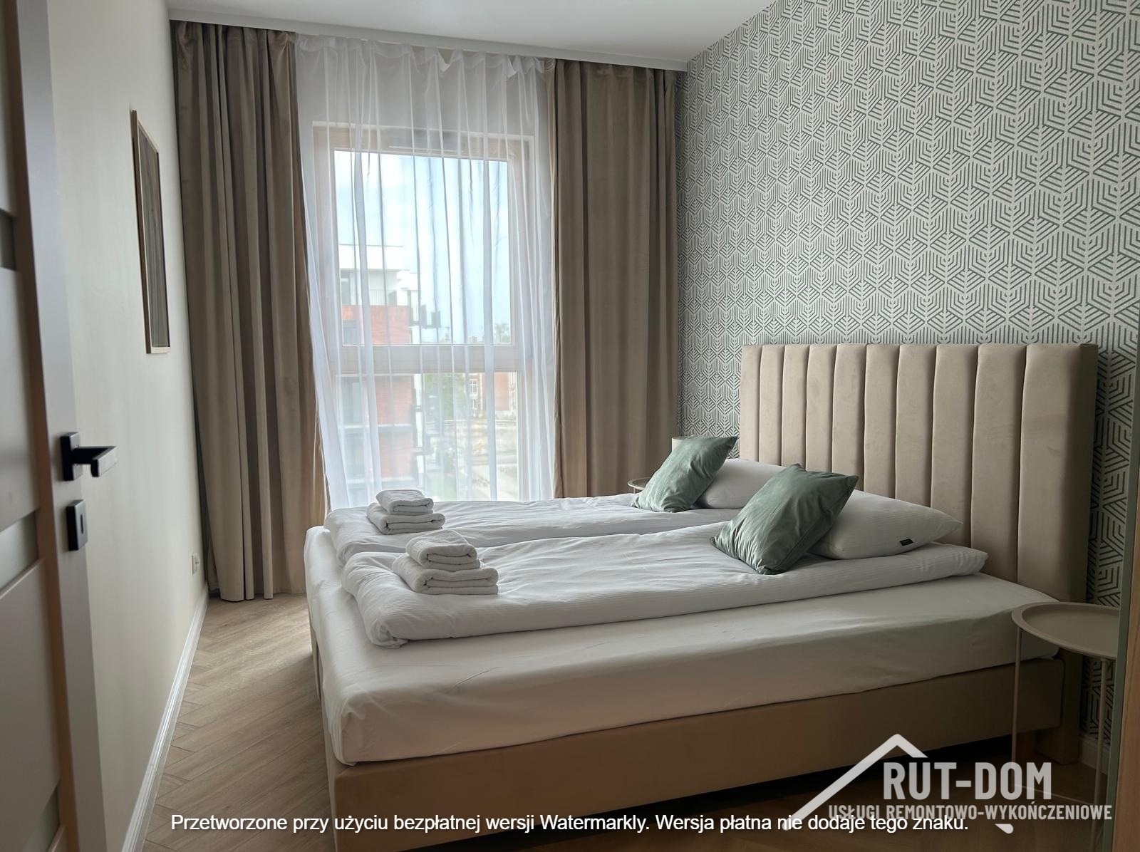 Jasna sypialnia z dwoma łóżkami, beżowym zagłówkiem i wzorzystą tapetą. Widok na okno z zasłonami. Minimalistyczny design z akcentami kolorystycznymi w postaci poduszek.