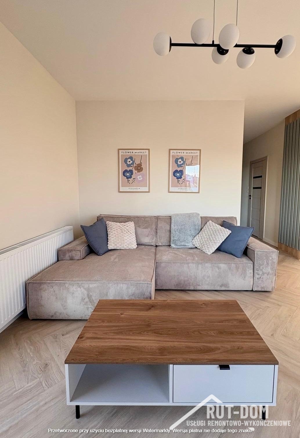 Jasny salon z narożną sofą w prążki, drewnianym stolikiem kawowym z białą szufladą i dwoma plakatami 'Flower Market' nad sofą. Nowoczesne oświetlenie sufitowe.