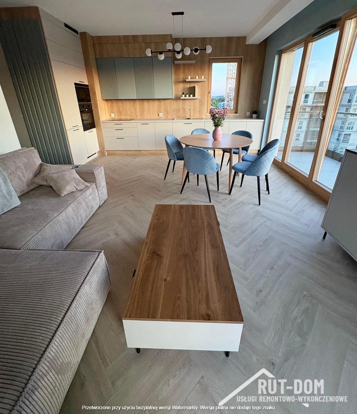 Jasne, przestronne wnętrze po remoncie: parkiet w jodełkę, nowoczesna kuchnia z drewnianymi akcentami i okno z widokiem na budowę. Minimalistyczny salon z sofą i stolikiem kawowym.