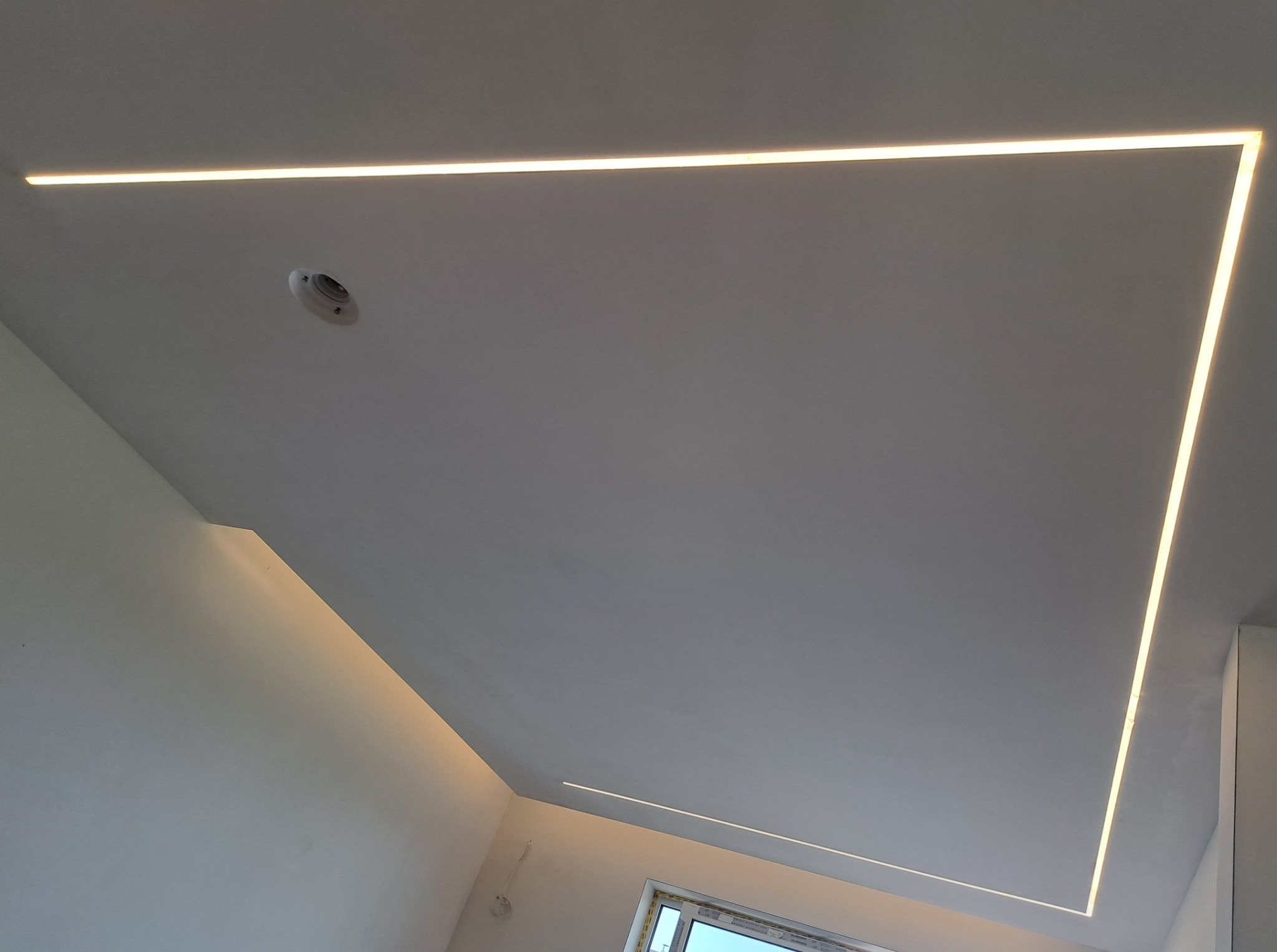 Nowoczesne oświetlenie sufitowe LED w kształcie prostokąta, wkomponowane w gładką, białą powierzchnię sufitu, z widocznym punktem oświetleniowym.