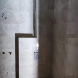 Wnętrze łazienki w trakcie remontu: widoczne płytki imitujące marmur, wystające rury, zamontowany stelaż podtynkowy WC i włącznik światła.