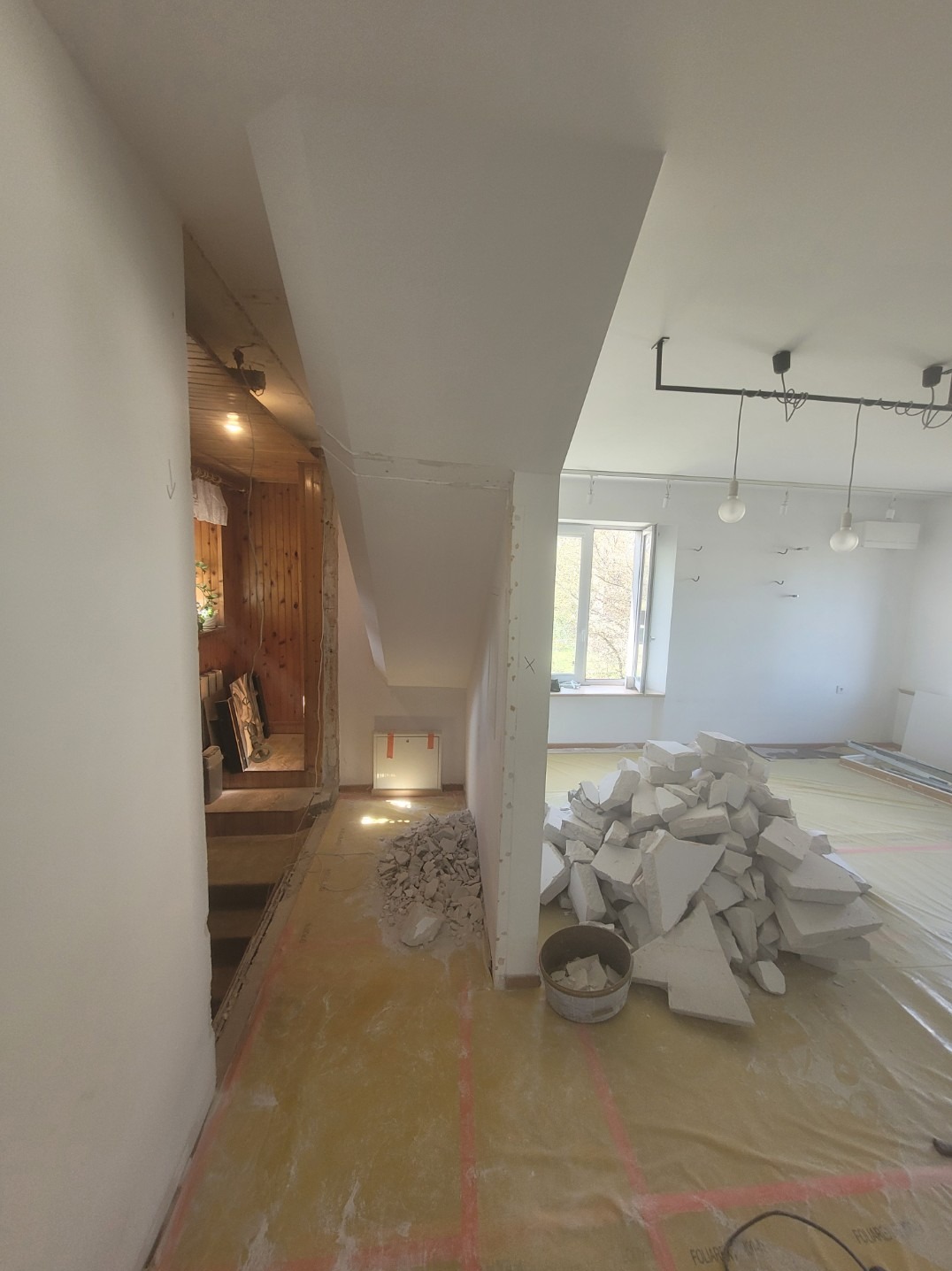 Wnętrze w trakcie demontażu: widoczne fragmenty ścian, gruz, podłoga zabezpieczona folią. Część pomieszczenia w surowym stanie, druga po demontażu.