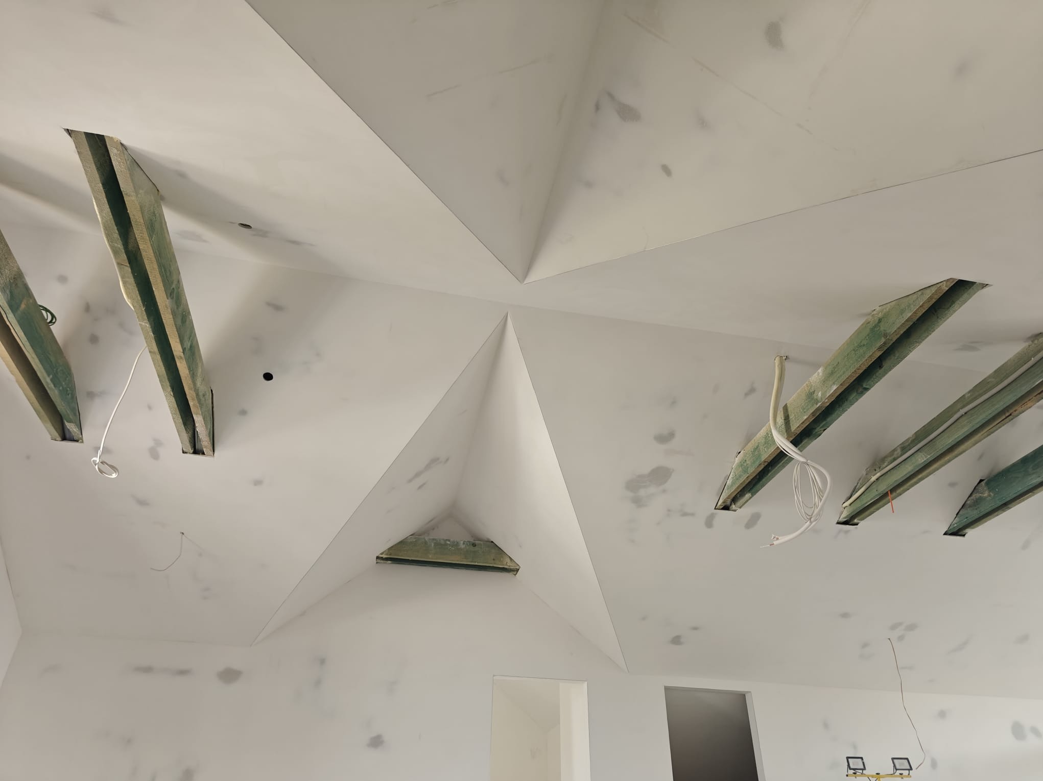 Skośny sufit poddasza po szpachlowaniu, z widocznymi drewnianymi belkami i śladami po łatach. Przygotowanie do malowania, surowe wykończenie.