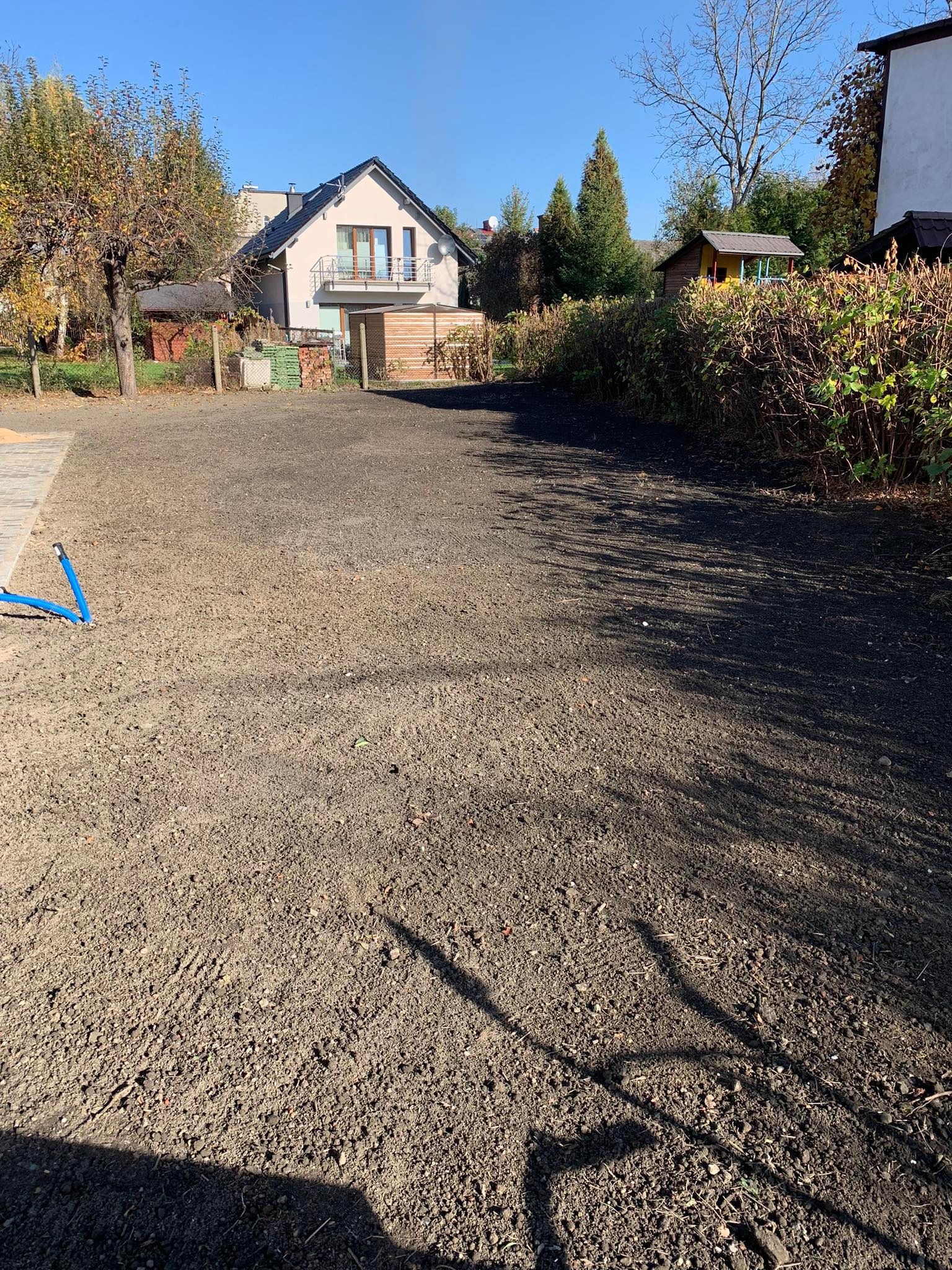 Przygotowany teren pod trawnik, widoczne rury nawadniające, dom jednorodzinny w tle.