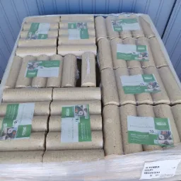 Paleta brykietu drzewnego SECA, owinięta folią stretch, z widocznymi etykietami informacyjnymi o wadze 10 kg i logo producenta, na tle szarej ściany hali.