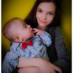 Portret dziewczynki trzymającej niemowlę z czerwoną muszką na tle żółtej ściany w Olecku.