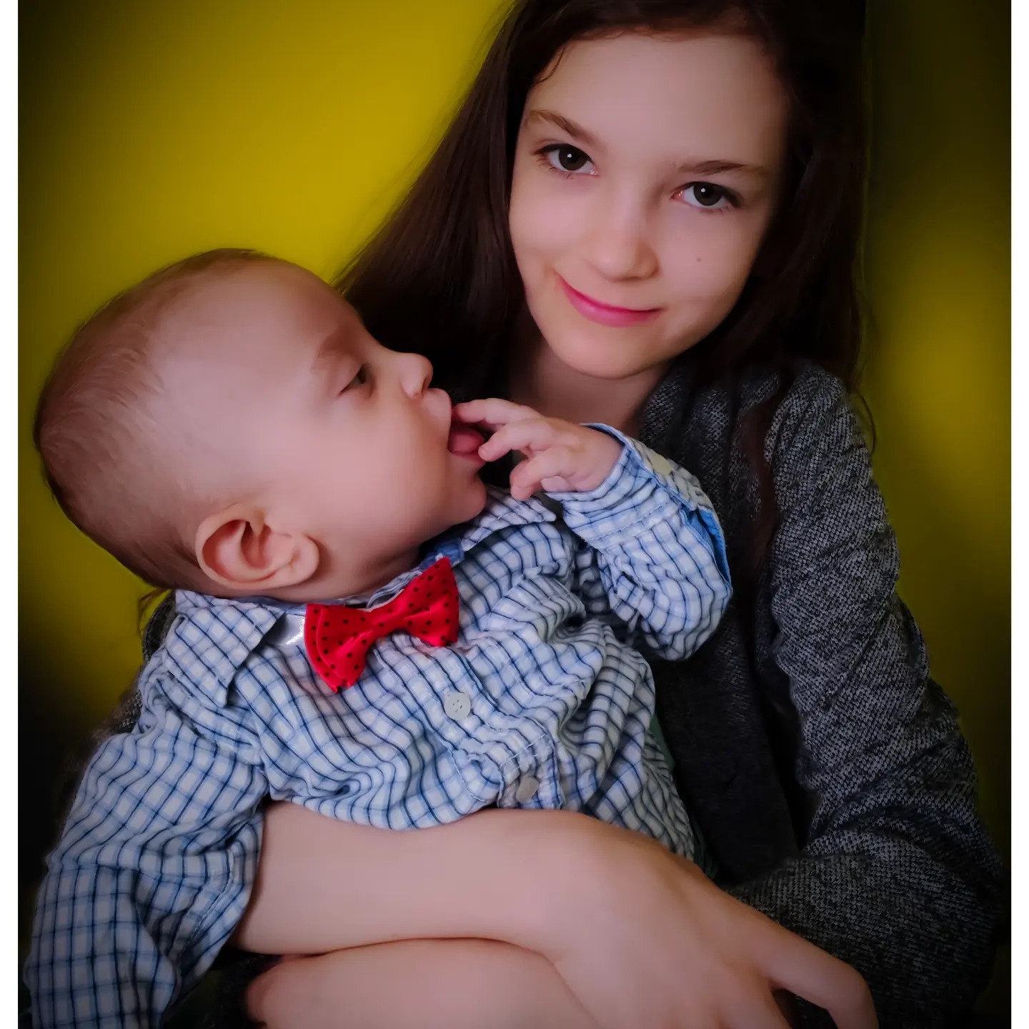 Portret dziewczynki trzymającej niemowlę z czerwoną muszką na tle żółtej ściany w Olecku.