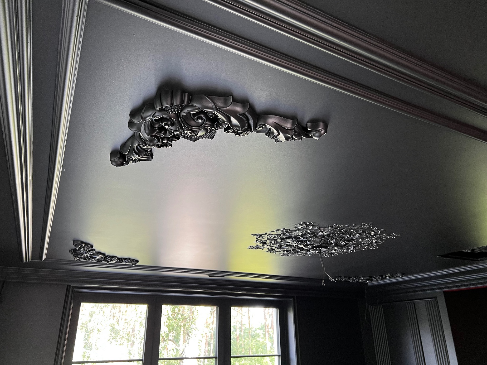 Czarne, pomalowane ozdobne sztukaterie na suficie w pokoju. Klasyczny wystrój wnętrza z oknem i ciemnymi ścianami. Dekoracyjne wykończenie sufitu.