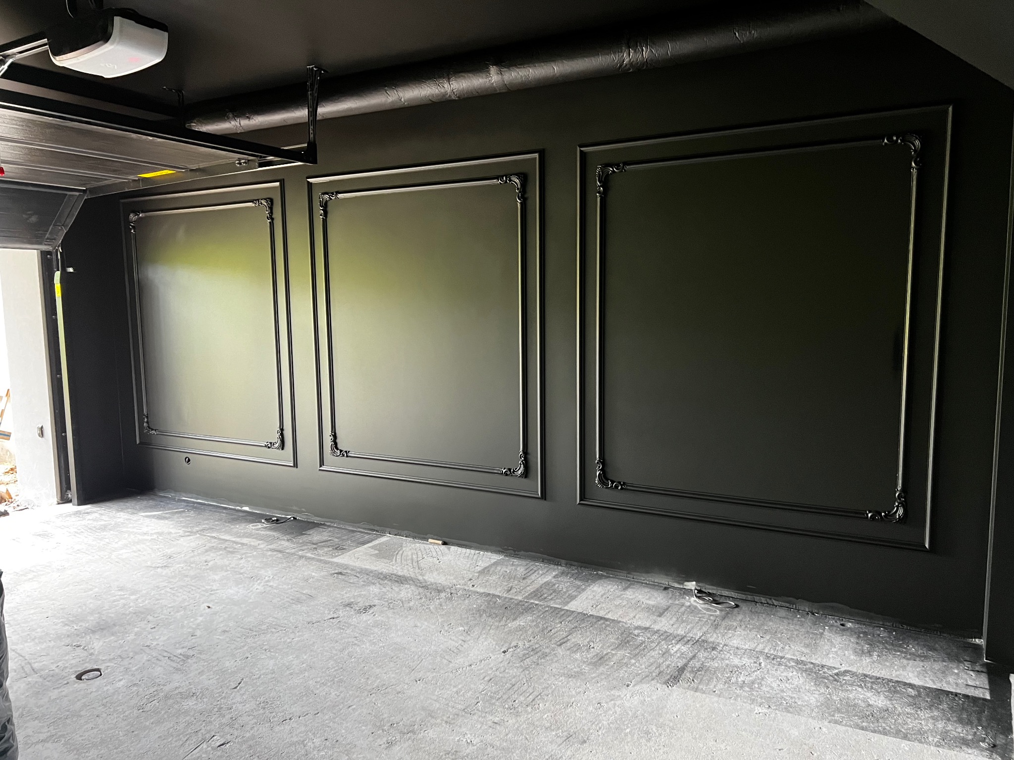 Eleganckie, ciemne panele ścienne z ozdobnymi ramami w wyremontowanym garażu. Widoczny surowy beton na podłodze i instalacja pod sufitem.