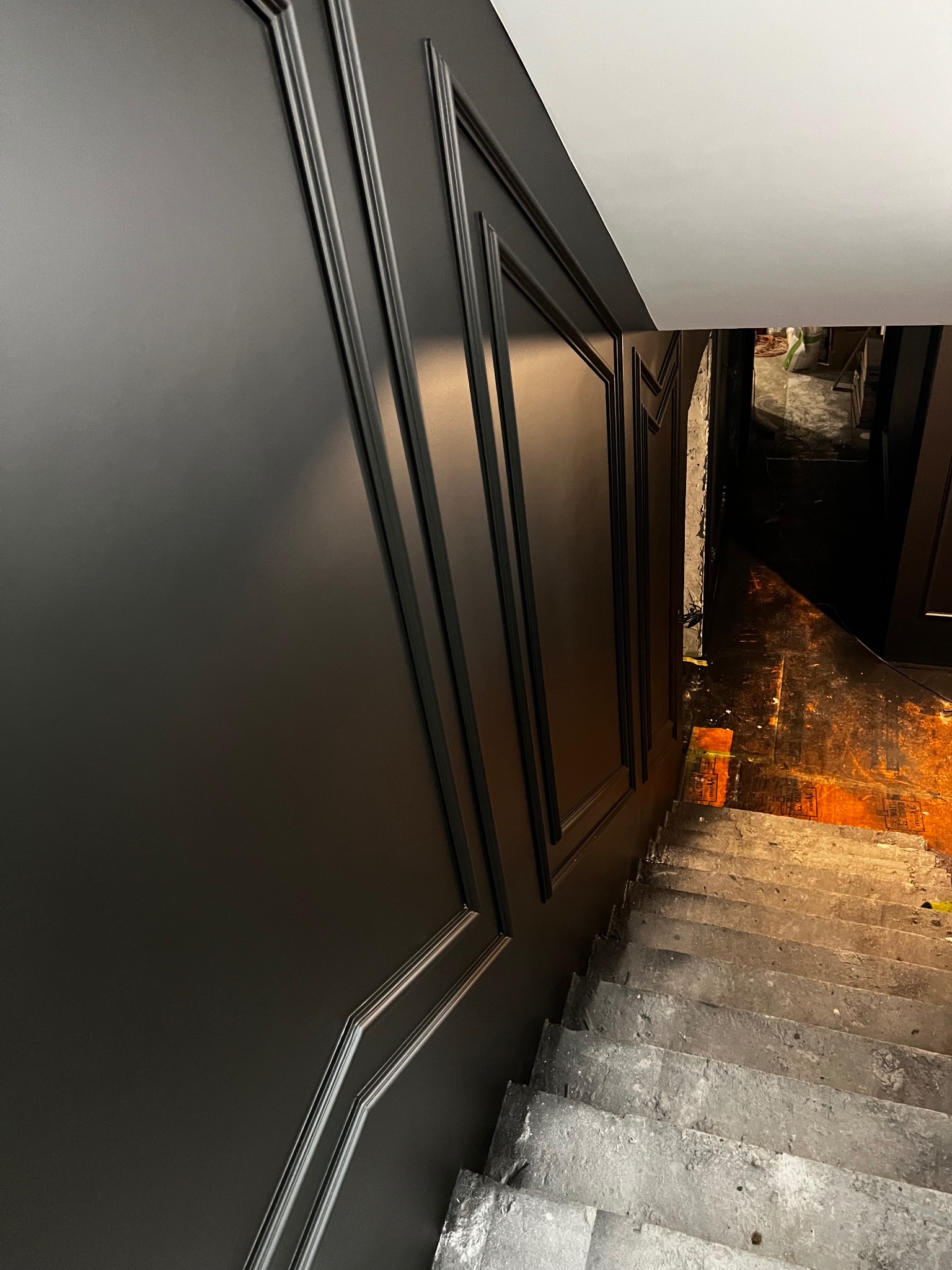Eleganckie, czarne panele ścienne z listwami dekoracyjnymi w korytarzu w Warszawie. Widok na schody w trakcie remontu, wysoki połysk.