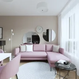 Jasny salon z pudrowo-różową sofą narożną, okrągłymi lustrami na ścianie i białym dywanem shaggy. Na stoliku marmurowym leżą książki i magazyn. W tle widoczna biała jadalnia i czarna komoda.
