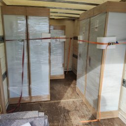 Erni Transport - Meble zabezpieczone folią i pasami transportowymi wewnątrz samochodu dostawczego, widoczne koce zabezpieczające na podłodze.
