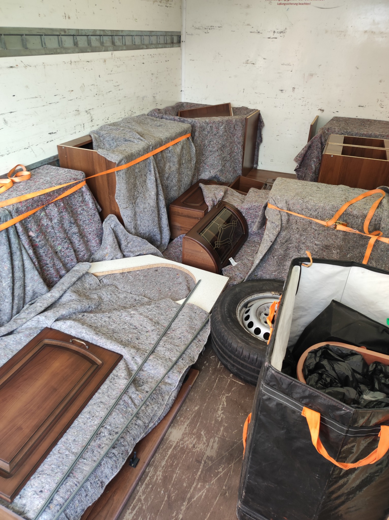 Meble zabezpieczone kocami i pasami transportowymi wewnątrz przestrzeni ładunkowej, widoczne elementy demontażu i przygotowania do transportu, w tle ściana przestrzeni ładunkowej.
