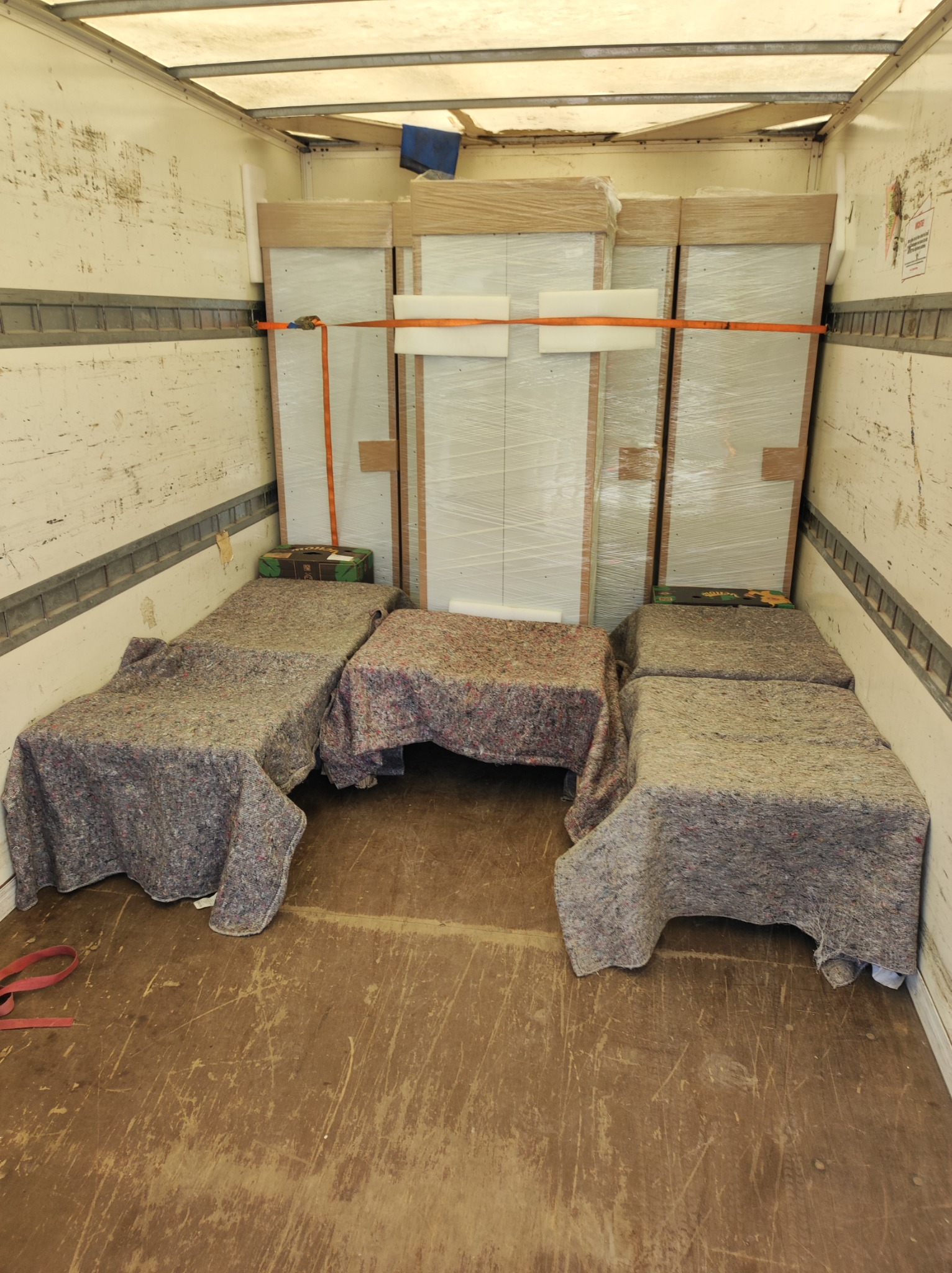 Wnętrze brudnej furgonetki załadowanej meblami zabezpieczonymi folią i pasami transportowymi, dodatkowo osłonięte szarymi kocami transportowymi.