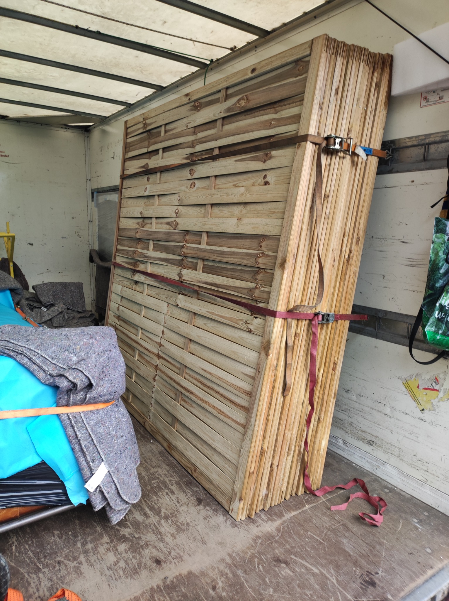 Panele ogrodzeniowe zabezpieczone pasami transportowymi wewnątrz pojazdu dostawczego, widoczne koce ochronne.