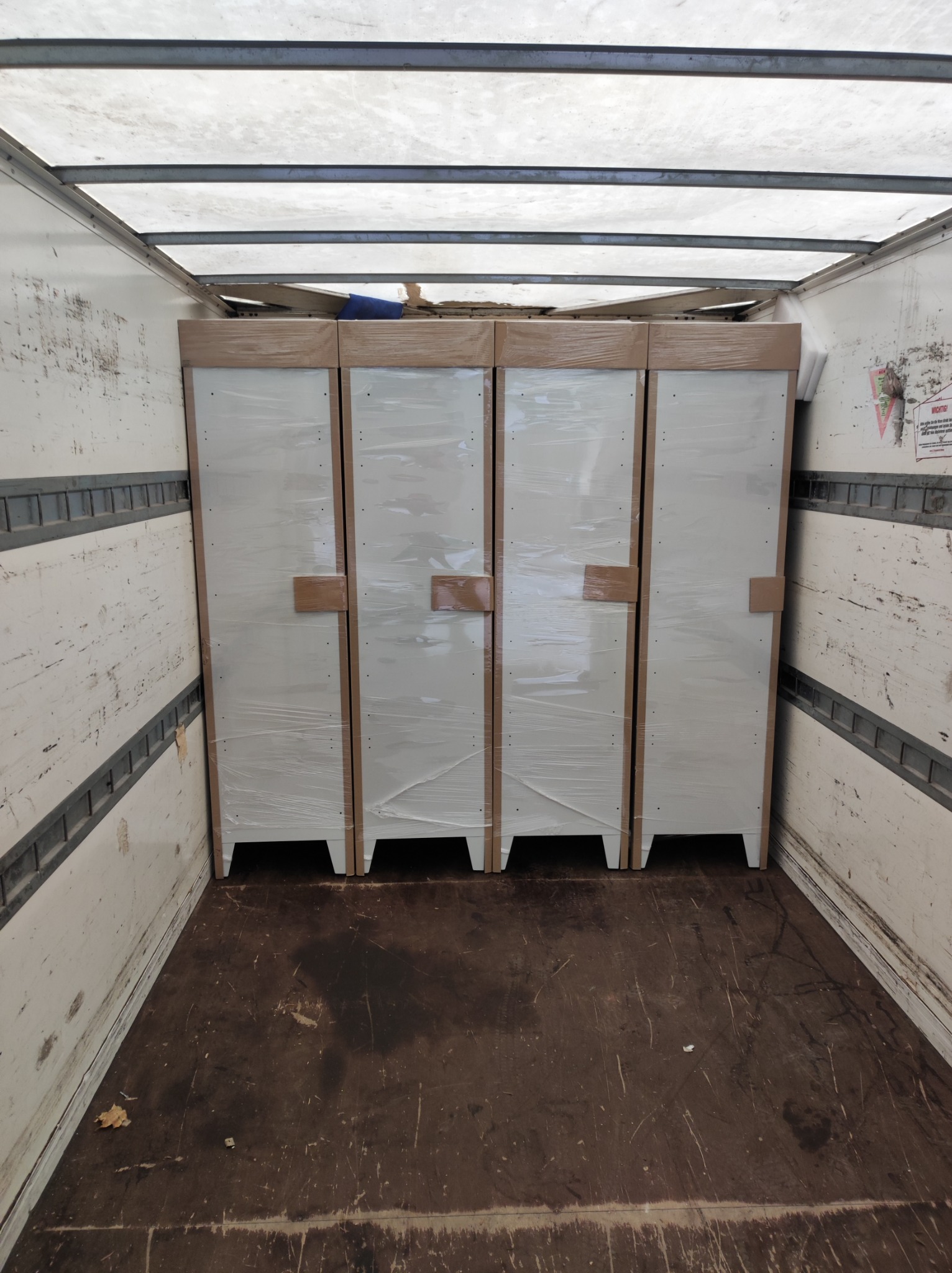 Cztery szafki w folii stretch, zabezpieczone podczas transportu wewnątrz przestrzeni ładunkowej z widoczną podłogą i ścianami pojazdu.