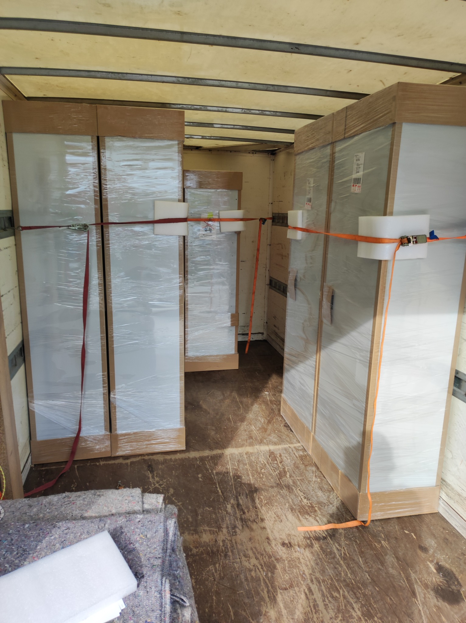 Meble zabezpieczone folią i pasami transportowymi wewnątrz samochodu dostawczego, widoczne koce zabezpieczające na podłodze.