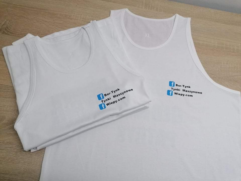 Dwa białe podkoszulki z nadrukowanym logo firmy Bor-Tynk Tynki Maszynowe i adresem strony internetowej Wiepy.com, leżące na drewnianym blacie.