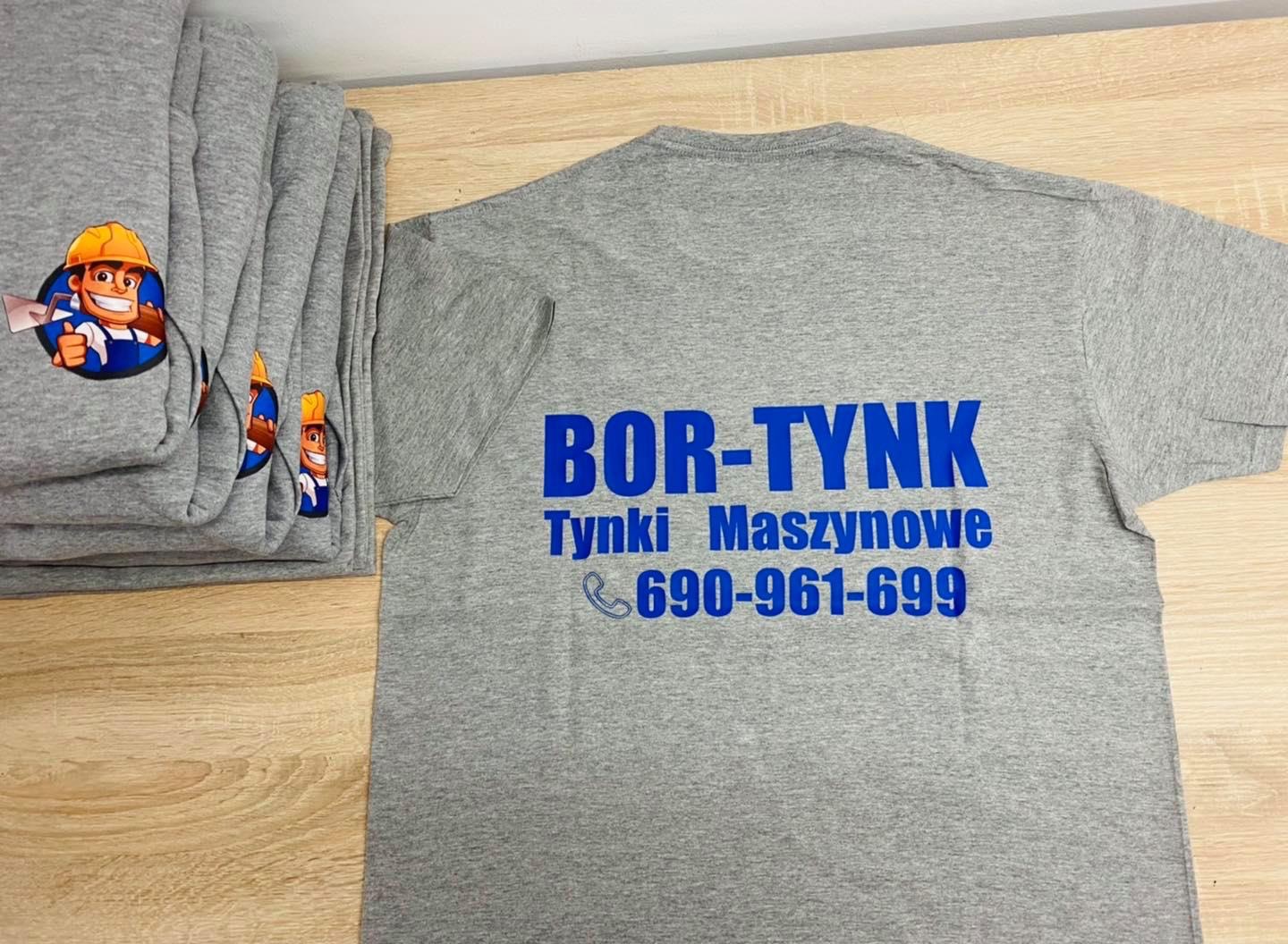 Stos szarych bluz i koszulek z niebieskim nadrukiem 'BOR-TYNK Tynki Maszynowe 690-961-699' oraz rysunkiem uśmiechniętego budowlańca w kasku.