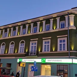 Zielony budynek banku BNP Paribas z podświetloną elewacją, widoczny wieczorem z perspektywy ulicy.