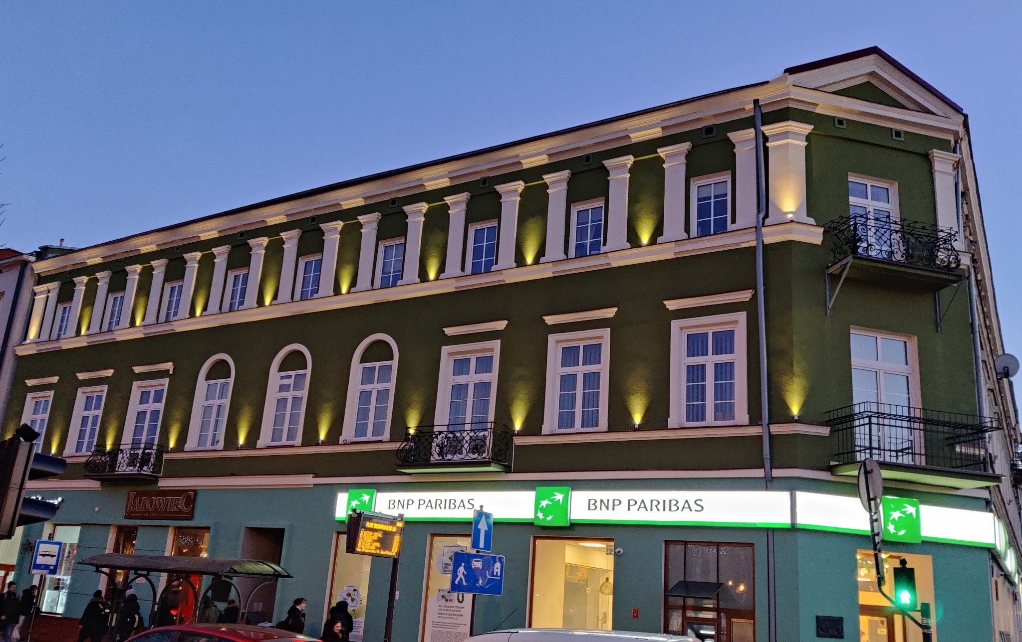 Zielony budynek banku BNP Paribas z podświetloną elewacją, widoczny wieczorem z perspektywy ulicy.
