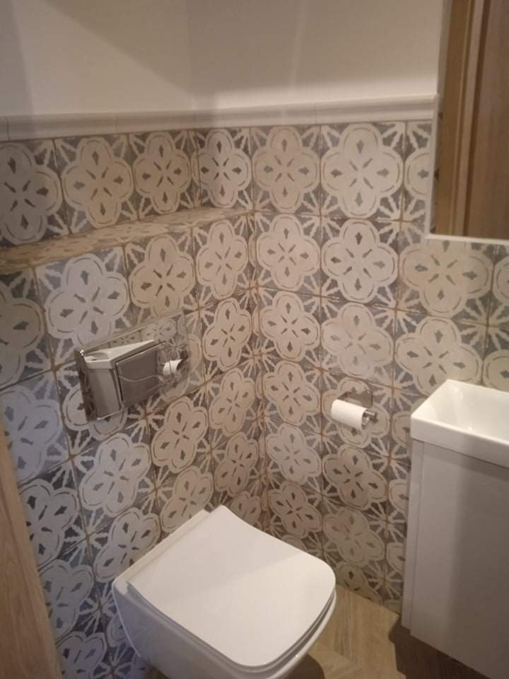 Wykończona łazienka z toaletą wiszącą i umywalką nablatową, ściany wyłożone dekoracyjnymi płytkami w kwiatowy wzór, z widocznym podajnikiem na papier toaletowy i uchwytem na papier.