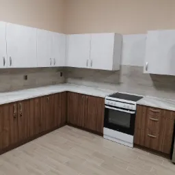 Nowoczesna kuchnia w kształcie litery L z białymi górnymi szafkami i dolnymi szafkami w kolorze drewna, marmurowy blat i płytki imitujące drewno na ścianie i podłodze, wraz z białą kuchenką...