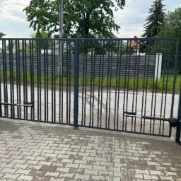 Nowoczesna, metalowa brama wjazdowa z automatyką, widoczny siłownik, kostka brukowa na podjeździe.