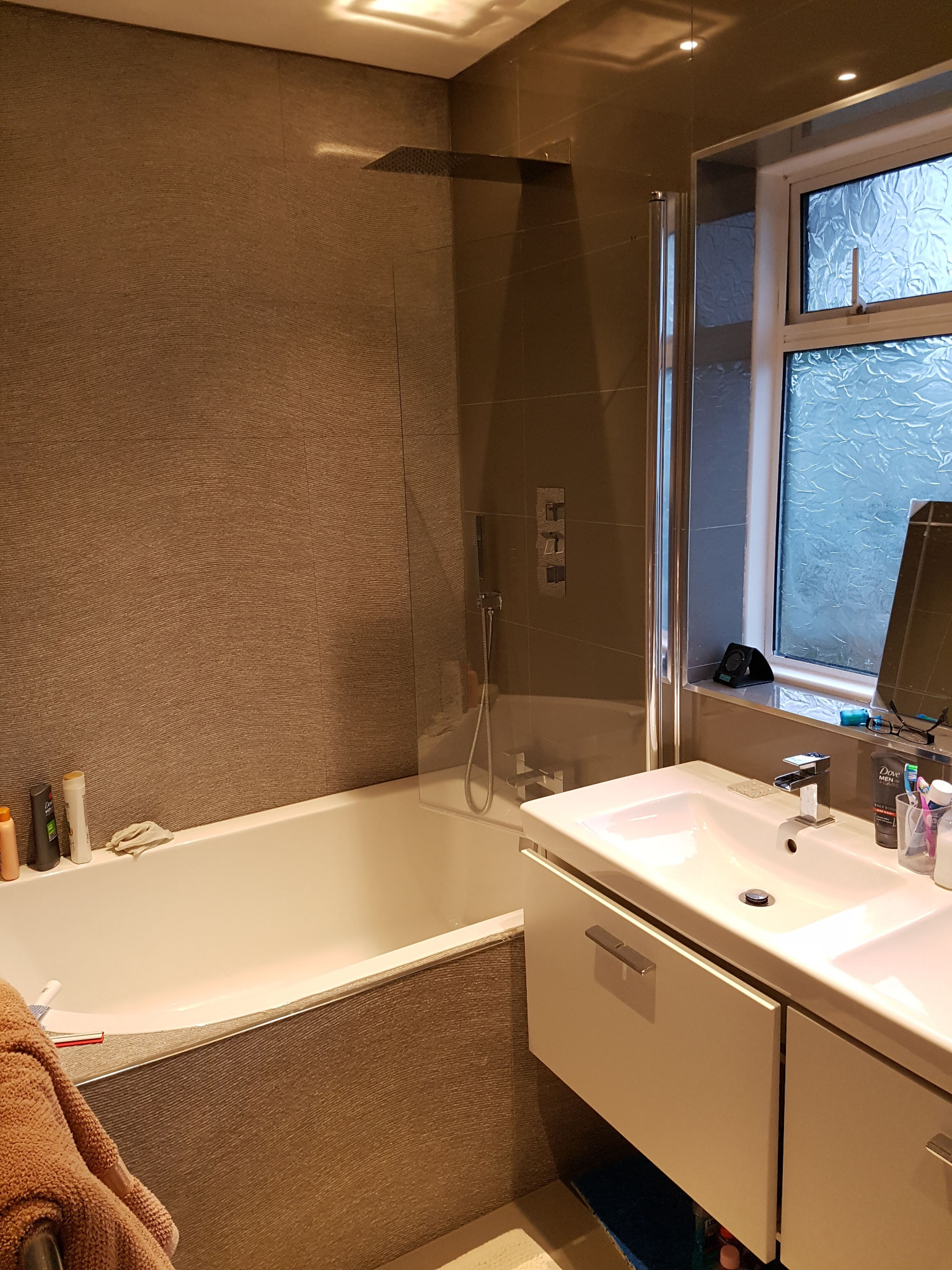 Nowoczesna łazienka z wanną, deszczownicą, umywalką nablatową i oknem z matową szybą, wykończona szarą płytką imitującą tkaninę.